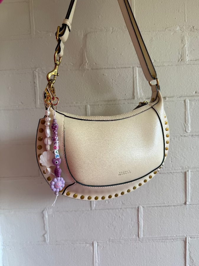 Beige handbag with decorative elements against a white brick wall
