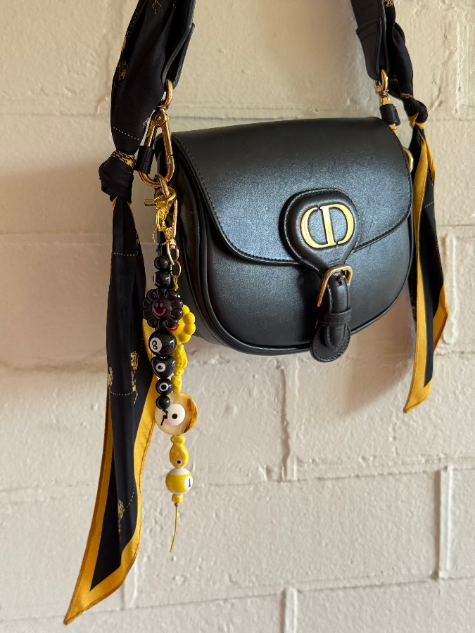 Black handbag with yellow accents on a textured white wall