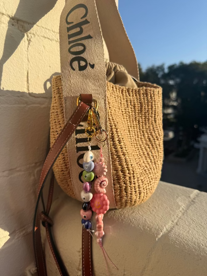Woven handbag with 'Chloe' branding and a colorful keychain on a textured surface.