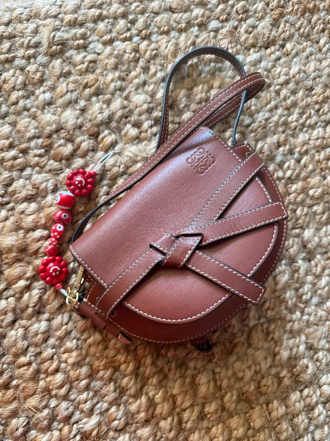 This image features an elegant strawberry-shaped handbag, crafted with a smooth, rich brown leather. The handbag boasts a classic design with a compact, rounded shape and is accented with a stylish buckle strap detail.