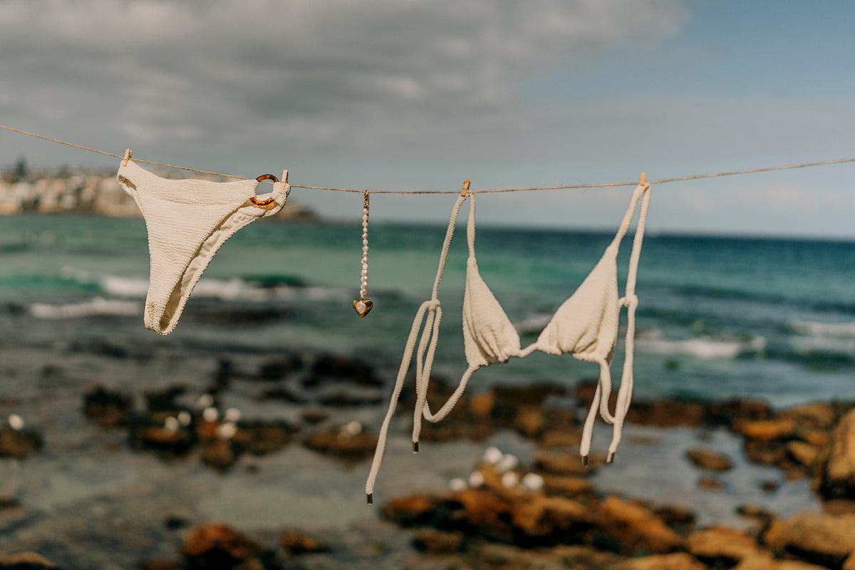 White bikini hanging on a clothesline with ocean and rocks in the background