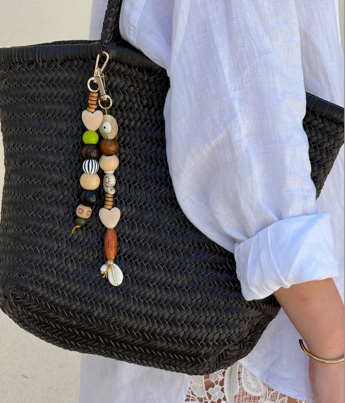 Black woven bag with a decorative keychain featuring beads and a shell, held by a person wearing a white shirt.