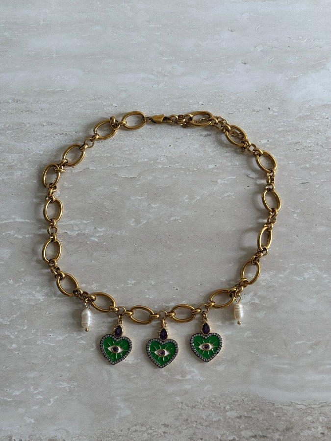 A gold stainless steel chain necklace with gold stainless steel charms and freshwater pearls, featuring a heart-shaped charm in green and a floral charm in purple.