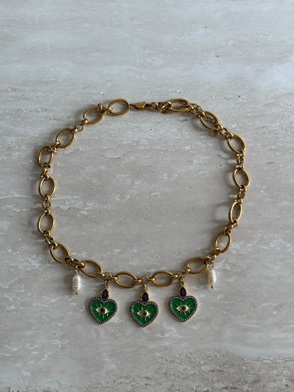 A gold stainless steel chain necklace with gold stainless steel charms and freshwater pearls, featuring a heart-shaped charm in green and a floral charm in purple.