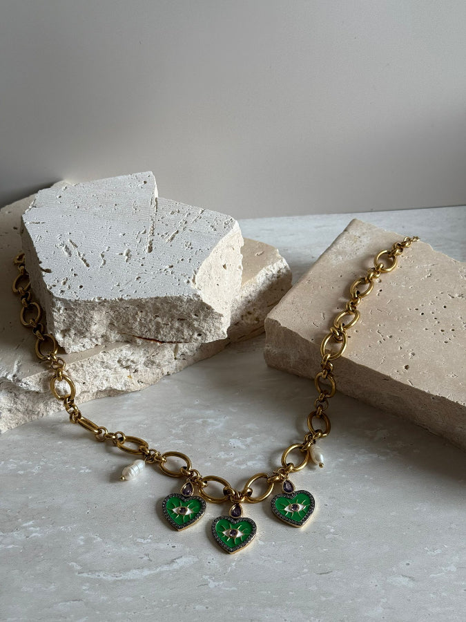 Gold bracelet with green heart charms on a textured surface