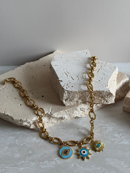 A gold stainless steel chain necklace with two gold stainless steel charms, one with a blue eye-shaped design and the other with a sunflower pattern.