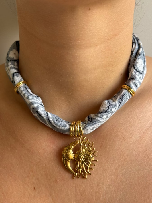 A person wearing a paisley bandana style necklace with a gold stainless steel charm.