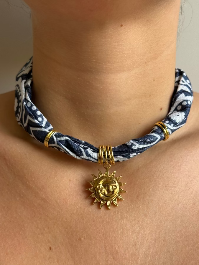A person wearing a blue and white paisley bandana necklace with a gold stainless steel charm.