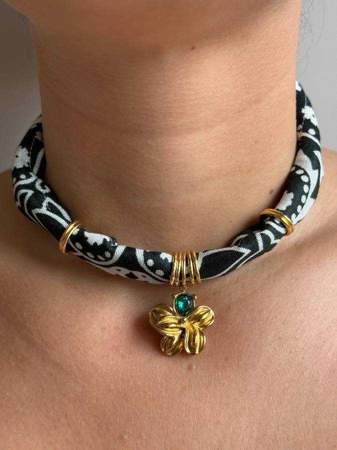 A person wearing a black and white paisley bandana necklace with a gold stainless steel charm.