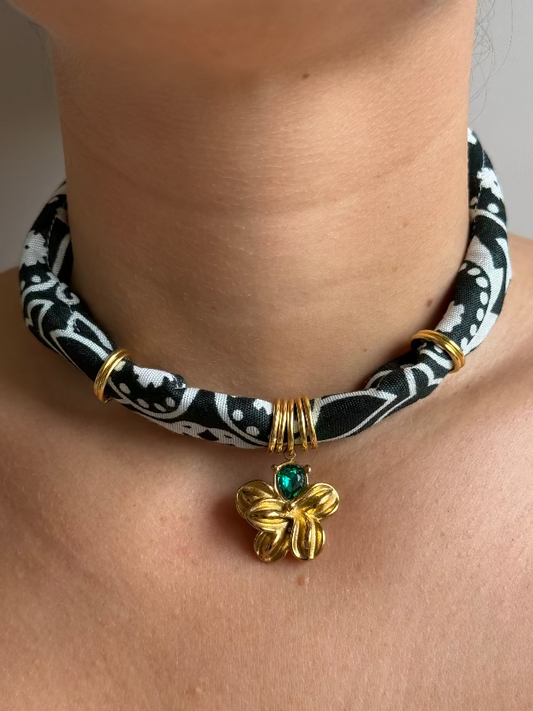A person wearing a black and white paisley bandana necklace with a gold stainless steel charm.