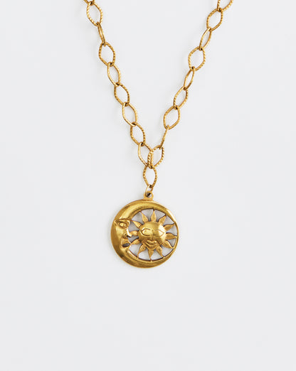 Gold necklace with a sun and moon pendant on a white background