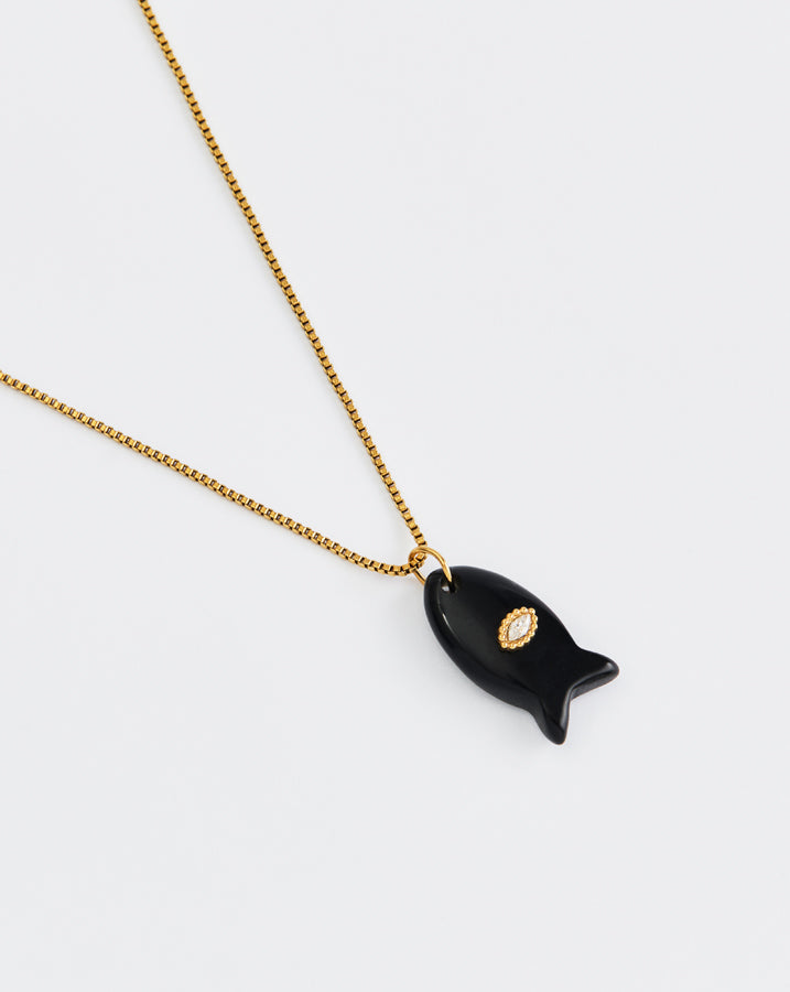 Black fish-shaped pendant on a gold chain against a white background