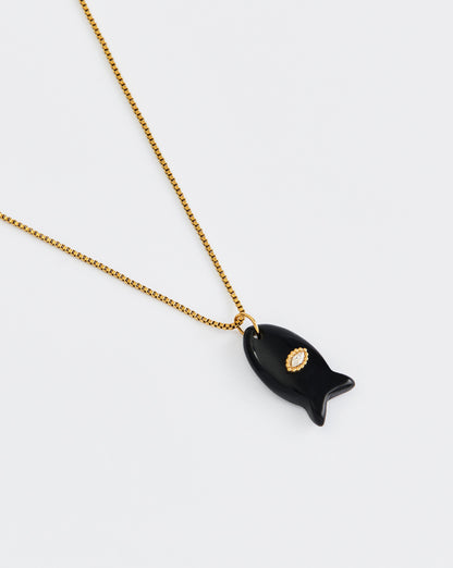 Black fish-shaped pendant on a gold chain against a white background